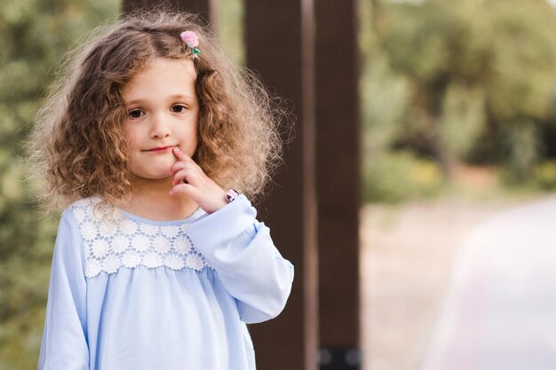 Jolie petite fille aux cheveux blonds bouclés posant à l'extérieur dans le parc