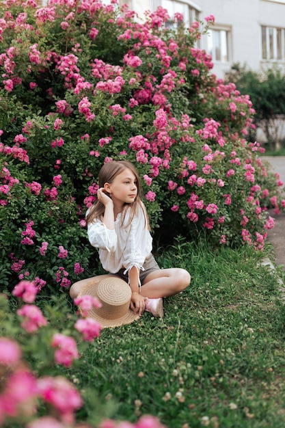 Jolie petite fille aux cheveux blonds dans un chapeau de paille Fleurs roses Été