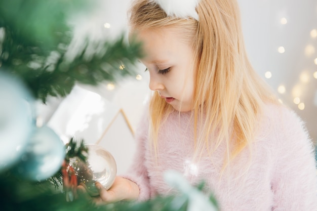 Jolie petite fille aux cheveux blonds décore un arbre de Noël