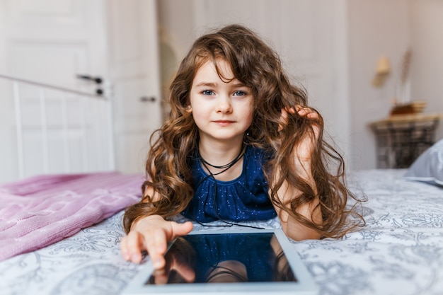 Jolie petite fille aux cheveux bouclés à l&#39;aide de tablette numérique