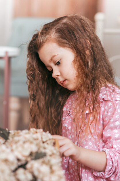 Une jolie petite fille aux cheveux fornic regarde les fleurs. Portrait vertical