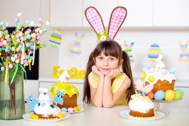 Une jolie petite fille aux oreilles de lapin prépare un gâteau de Pâques et des oeufs peints Fête religieuse