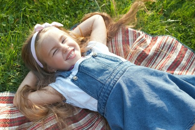 Jolie petite fille aux yeux fermés allongée sur l'herbe verte en été en faisant une sieste.