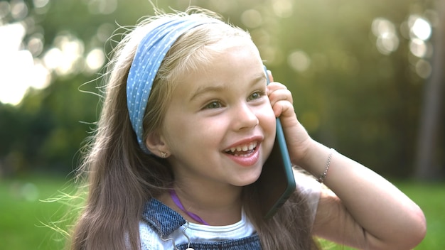 Jolie petite fille ayant une conversation sur son téléphone portable dans un parc d'été.