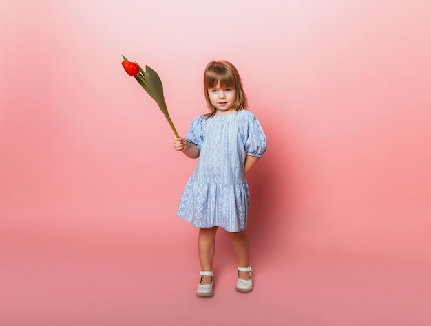 Jolie petite fille blonde avec un bouquet de tulipes dans une robe en coton sur fond rose 8 mars