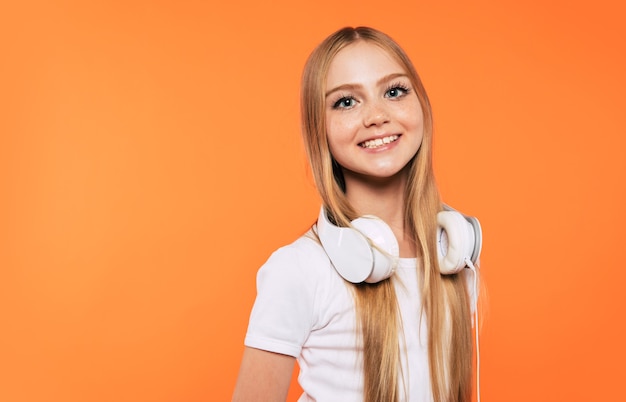 Jolie petite fille blonde émotionnelle dans les écouteurs s'amuse et danse sur fond jaune