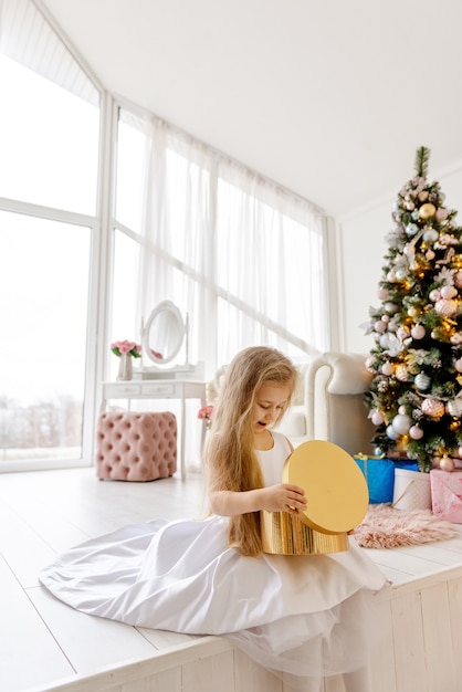 Jolie petite fille blonde ouvre un cadeau de Noël. Joyeux Noël bébé.