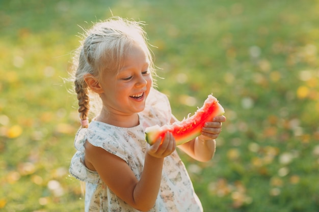 Jolie petite fille blonde avec pastèque sur l'herbe dans le parc.