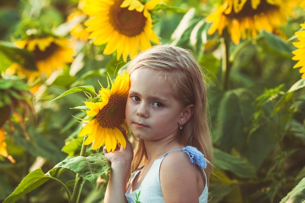 La jolie petite fille blonde a penché sa joue au tournesol sur le champ de tournesol