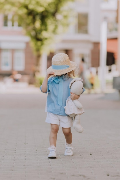 jolie petite fille blonde en robe bleue et chapeau de paille jouant près de la fontaine avec un lapin en peluche, carte