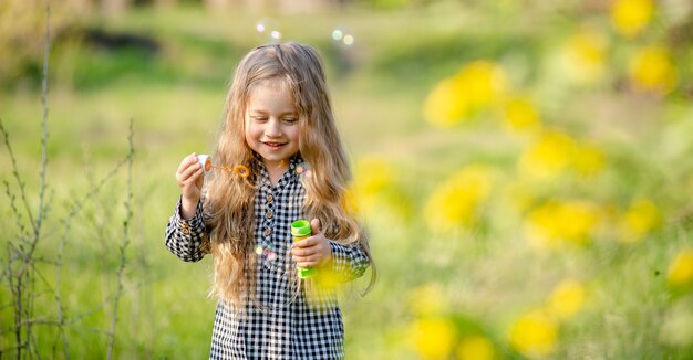 Jolie petite fille blonde soufflant des bulles de savon s'amusant dans le parc du printemps.