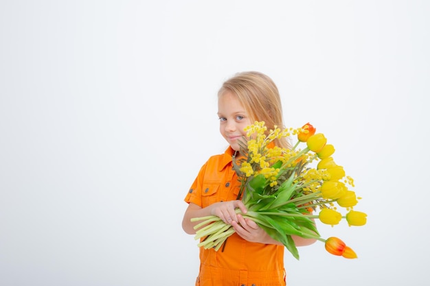 Jolie petite fille blonde vêtue d'une robe tenant un bouquet de fleurs printanières sur fond blanc