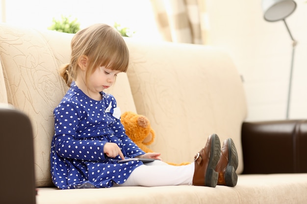 Jolie petite fille sur le canapé utilise un téléphone portable