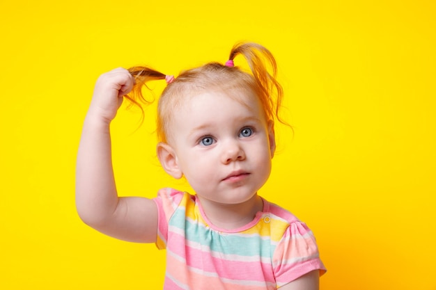 Jolie petite fille caucasienne avec des queues de cheval sur fond jaune