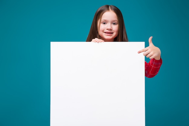 Jolie petite fille en chemise à carreaux aux cheveux bruns tient du papier clair