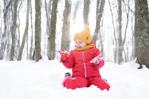 Jolie petite fille en combinaison de neige rose joue avec la neige dans la forêt d'hiver