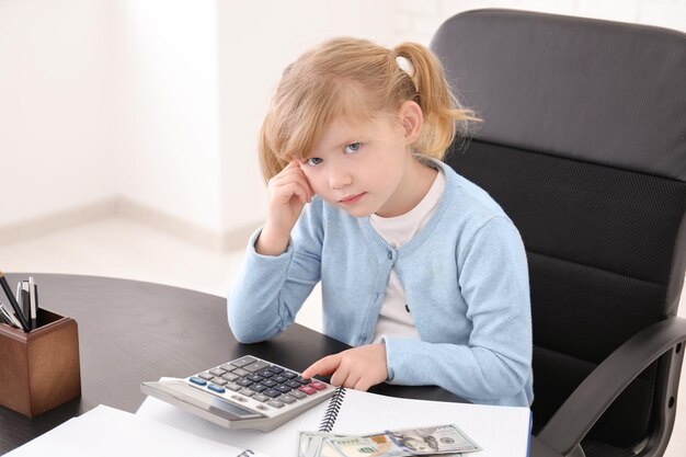 Jolie petite fille comptant de l'argent à table à l'intérieur