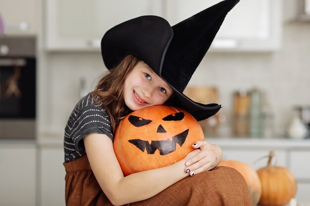 Jolie petite fille en costume de sorcière avec citrouille de sculpture