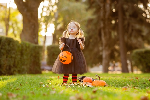 Une jolie petite fille en costume de sorcière se promène dans la rue avec un bonbon en forme de citrouille.