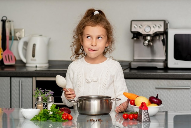 Une jolie petite fille cuisine dans la cuisine à partir de légumes frais.