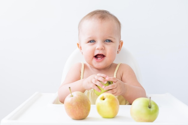 jolie petite fille dans une chaise bébé mangeant des pommes. Premier aliment solide pour bébé