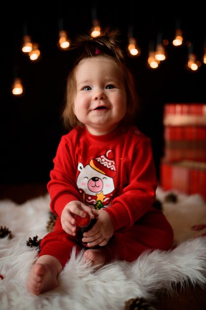 Jolie petite fille dans un costume de Noël rouge avec des guirlandes rétro est assis sur une fourrure