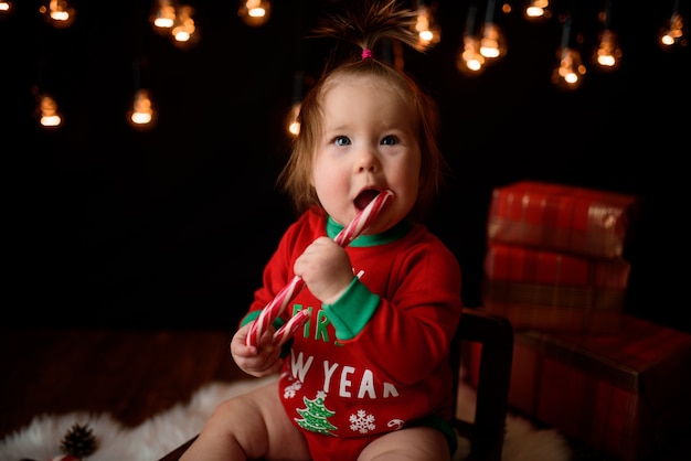 Jolie petite fille dans un costume de Noël rouge avec des guirlandes rétro est assis sur une fourrure