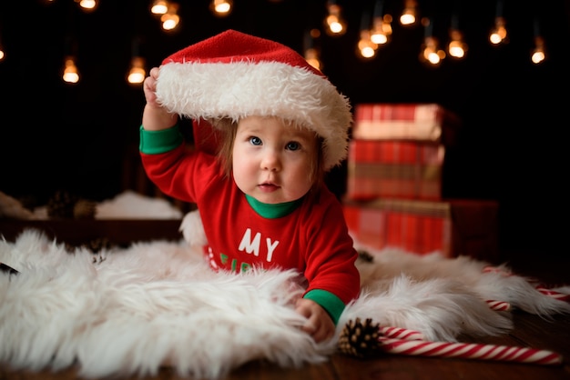 Jolie petite fille dans un costume de Noël rouge avec des guirlandes rétro est assis sur une fourrure