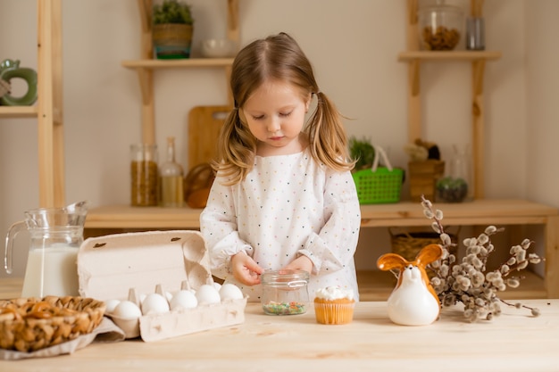 Jolie petite fille dans une robe en coton à la maison dans une cuisine en bois prépare un gâteau de Pâques