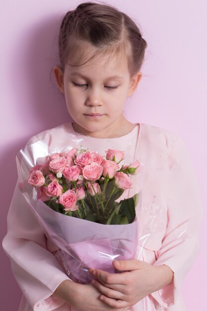 Une jolie petite fille dans une robe rose tient un bouquet de roses roses