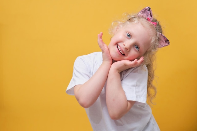 Jolie petite fille dans un t-shirt blanc s'amusant un enfant dans un bandeau avec des oreilles de chat sur fond jaune