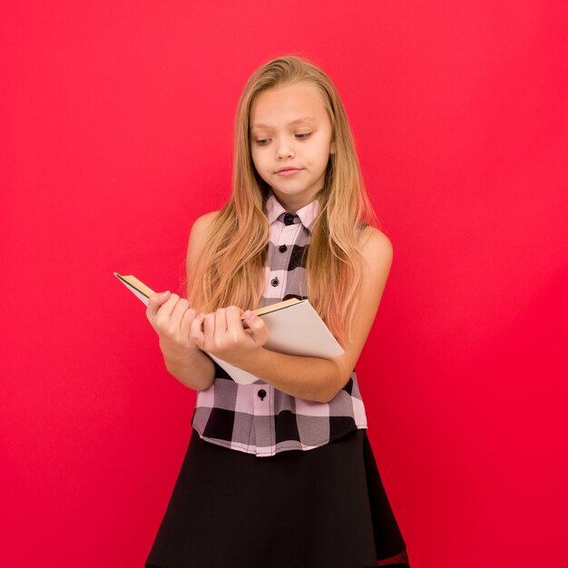 Jolie petite fille debout et livre de lecture sur rouge -