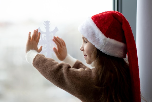 Une jolie petite fille décore les fenêtres avec des flocons de neige Ambiance de Noël du Nouvel An