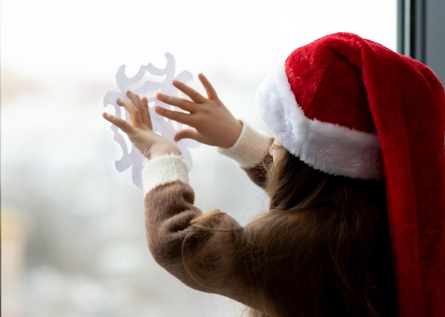 Une jolie petite fille décore les fenêtres avec des flocons de neige Ambiance de Noël du Nouvel An