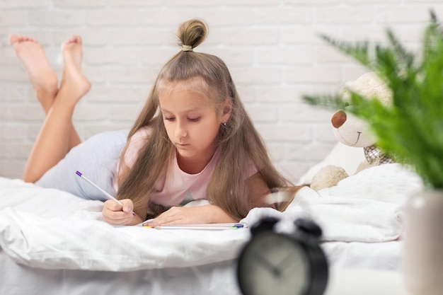 Photo jolie petite fille dessinant des images en position couchée sur le lit