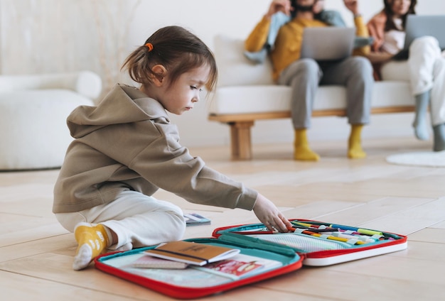 Jolie petite fille dessine dans le contexte des parents qui travaillent sur des ordinateurs portables à la maison