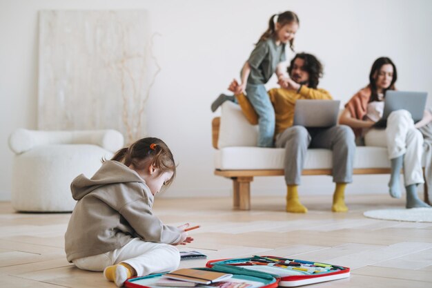 Jolie petite fille dessine dans le contexte des parents qui travaillent sur des ordinateurs portables à la maison