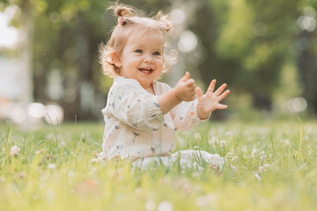 jolie petite fille avec une drôle de coiffure est assise sur une pelouse verte en fleurs dans le parc