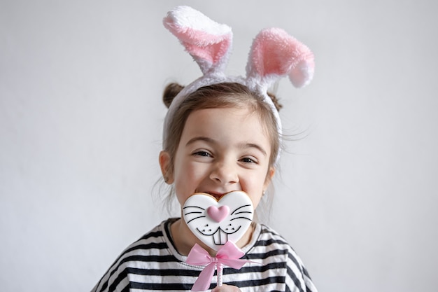 Jolie petite fille avec du pain d'épice de Pâques sur un bâton et des oreilles de lapin décoratives sur sa tête