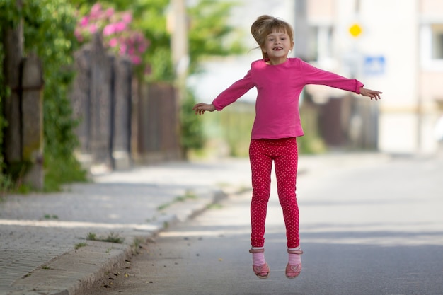 Jolie petite fille édentée souriante et drôle en vêtements de loisirs roses avec une longue queue de cheval blonde sautant