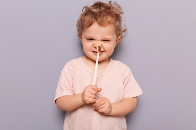 Jolie petite fille avec une émotion heureuse avec une brosse à dents dans sa petite main tout en posant sur fond gris importance des soins dentaires de l'enfance