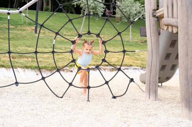 jolie petite fille enfant dans des vêtements colorés jouant sur l'aire de jeux pour enfants en été