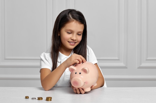 Jolie petite fille enfant mettant une pièce de monnaie dans la tirelire rose. enfant économisant de l'argent pour l'avenir