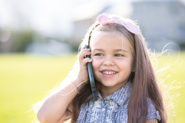 Jolie petite fille enfant parlant au téléphone portable souriant joyeusement à l'extérieur en été.