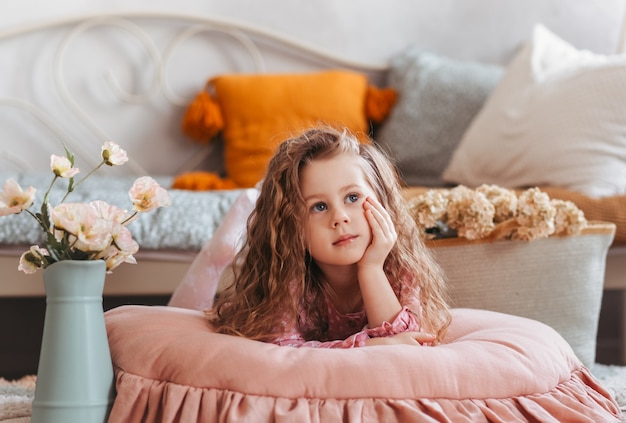 Une jolie petite fille est allongée sur le sol dans la chambre des enfants et rêve. Intérieur vintage