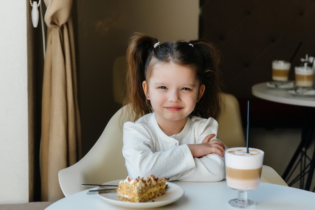 Une jolie petite fille est assise dans un café et regarde un gros plan de gâteau et de cacao. Régime alimentaire et nutrition adéquate.