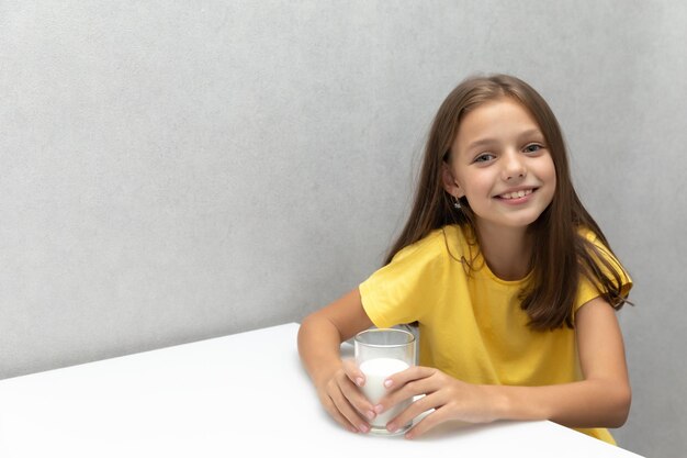 Jolie petite fille est assise avec un verre de lait près de la table et sourit Lait de ferme pour le petit déjeuner