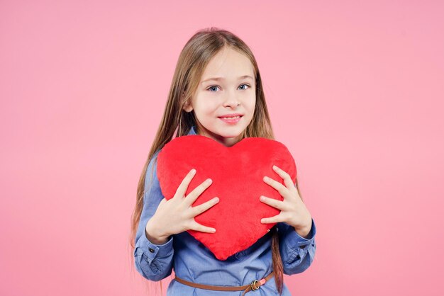 Jolie petite fille étreint fermement le gros coeur de jouet rouge