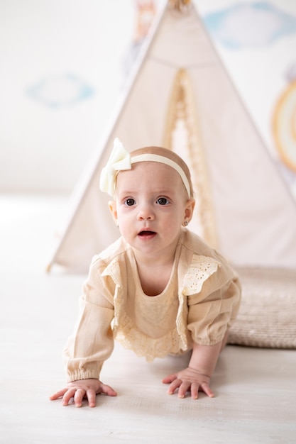Une jolie petite fille européenne aux yeux bruns dans un body beige en tissu naturel joue dans la chambre des enfants à la maison sur fond de wigwam et de jouets en peluche
