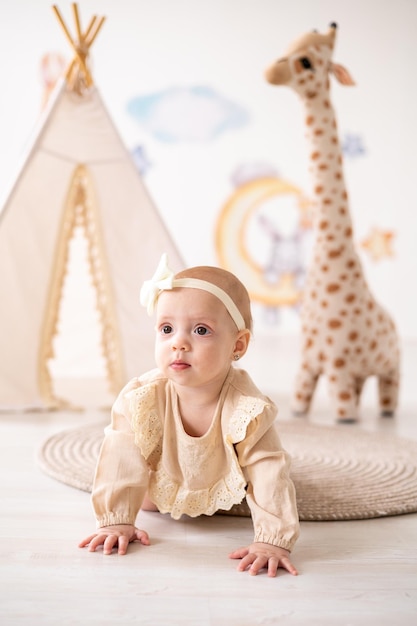 Une jolie petite fille européenne aux yeux bruns dans un body beige en tissu naturel joue dans la chambre des enfants à la maison sur fond de wigwam et de jouets en peluche